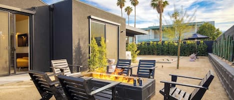 An outdoor patio with a fire pit, seating, and a view of a modern building.
