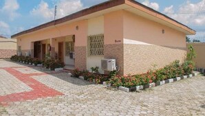 A single-story building with a flat roof, a covered porch, and a small garden area with flowers. - Classicus Inn Hotel (Ibadan)