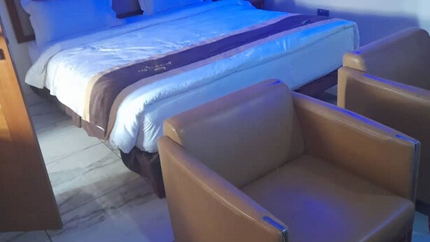 A bedroom with a bed, two leather armchairs, and a nightstand. - Classicus Inn Hotel (Ibadan)