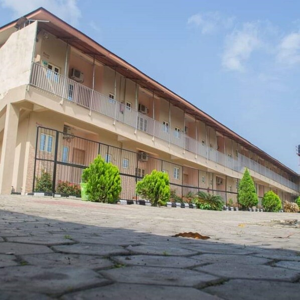 Un edificio de varios pisos con balcones, un patio empedrado y vegetación.