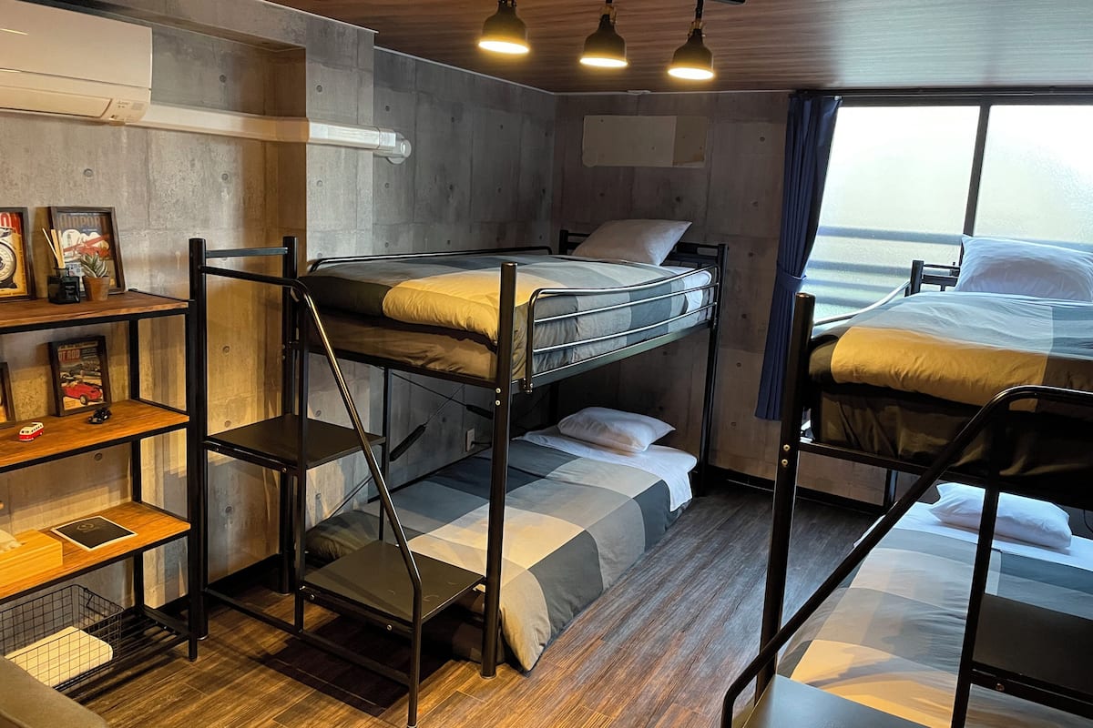 Dormitorio con literas, suelo de madera, literas de metal, un escritorio con silla y una ventana con cortinas.