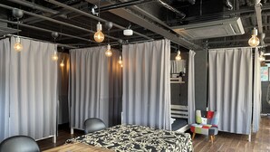 Habitación de hotel con una mesa de madera, una cama con colcha estampada, cortinas grises y lámparas colgantes.