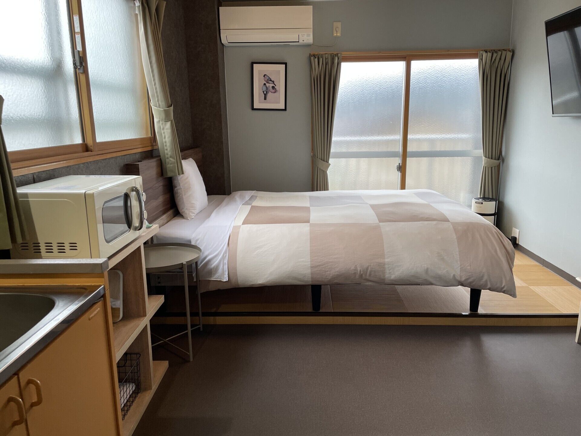 A hotel room with a bed, a microwave, a small table, a chair, a picture on the wall, and a window with curtains.