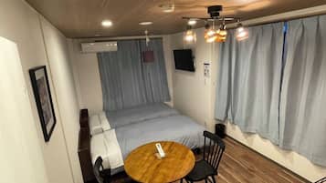 A compact hotel room with a single bed, a small round table with two chairs, a wooden floor, and a ceiling light fixture.