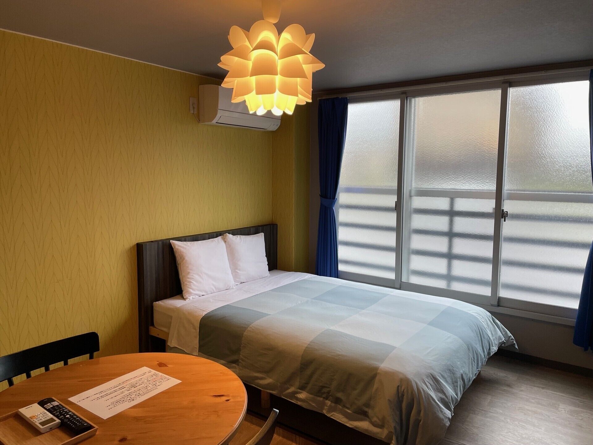 Una habitación de hotel con una cama, una mesa con una silla, una ventana con cortinas y una lámpara en el techo.