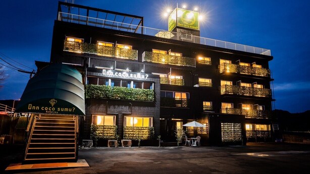 A multi-story building with balconies, a sign reading "Dann coco sumu?" and a water tank on the left.