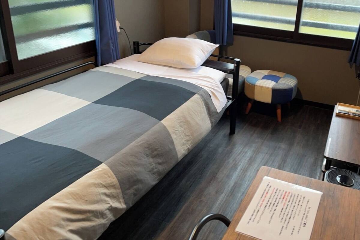 Habitación de hotel con cama, una mesita, una silla y ventana con cortinas.