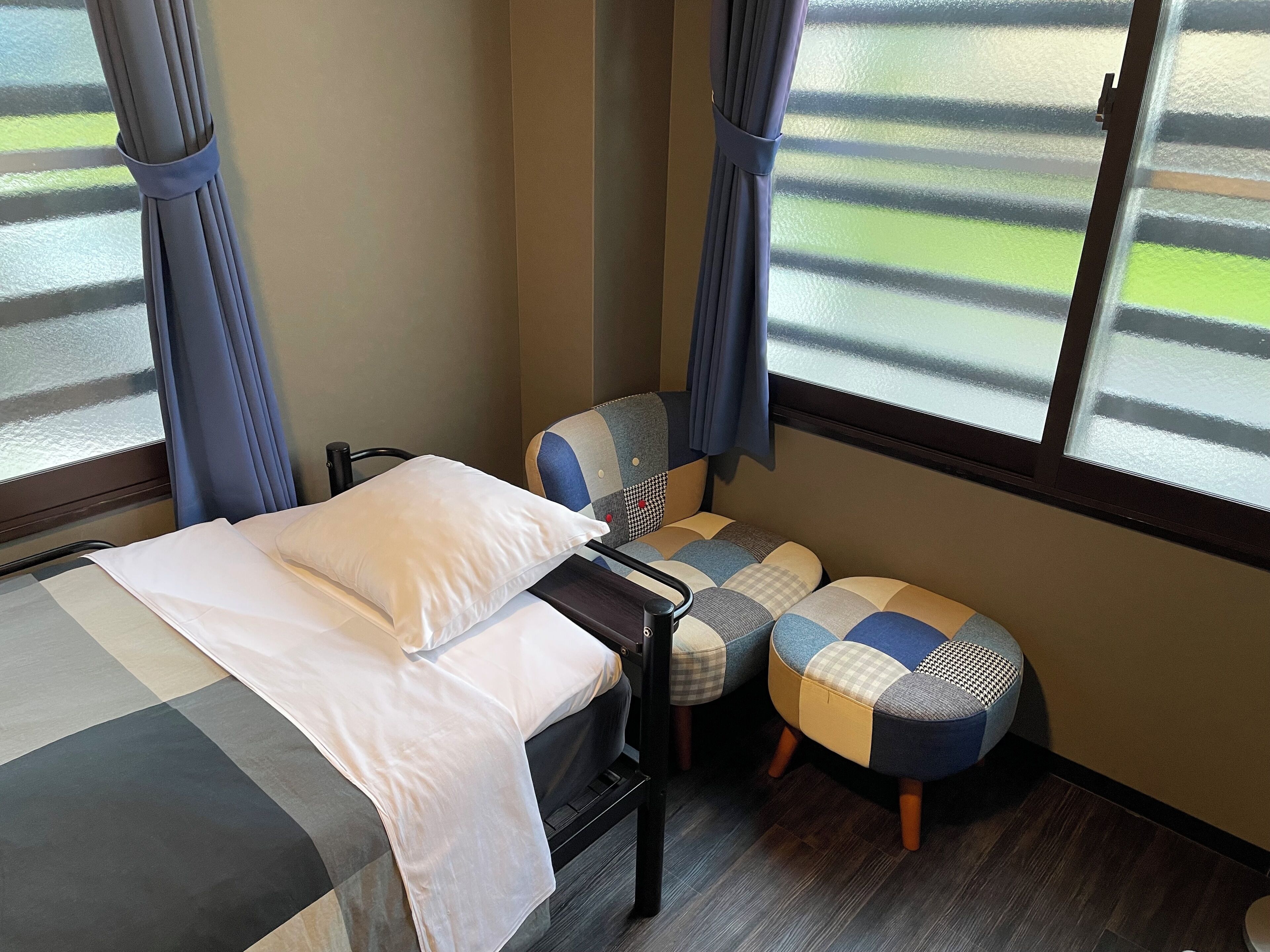A hotel room with a bed, a small table, a chair, and a window with curtains.