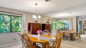 A dining room with a large wooden table, six chairs, and a chandelier. There are large windows with curtains, and a view of trees outside. - Marina Village 338 In Keowee Key (Salem)