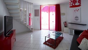 A modern living room with a staircase, a flat-screen TV, a glass coffee table, and a red sofa. - Playa Flor Chill Out Bungalows (Arona)