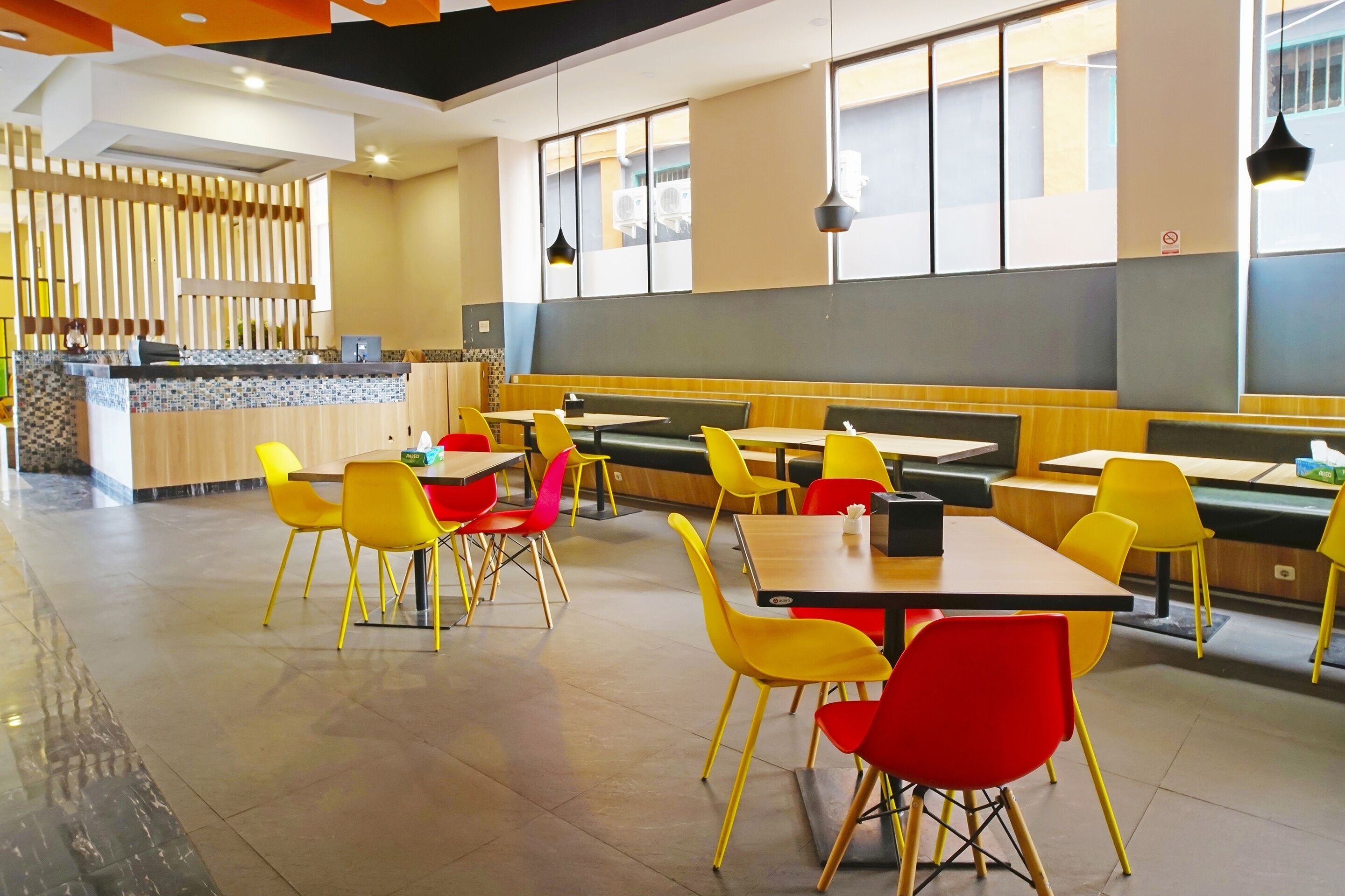 A modern restaurant with yellow and red chairs, a counter, and large windows.