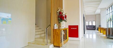 A modern hotel lobby with a wooden reception desk, a staircase, and a sofa in the background.