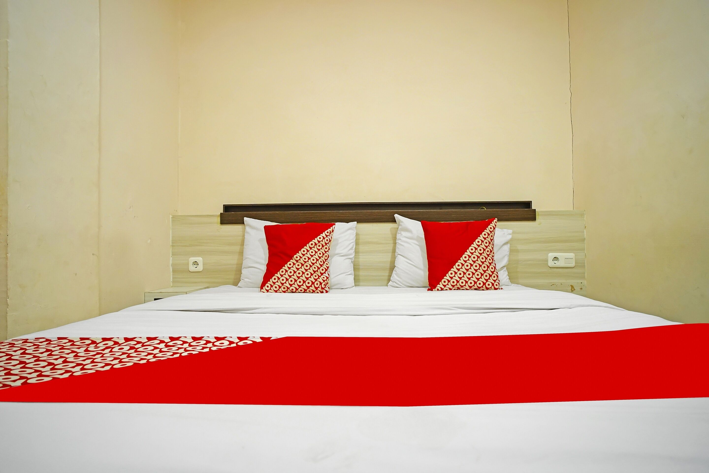 A neatly made bed with a red and white bedspread and patterned pillows.