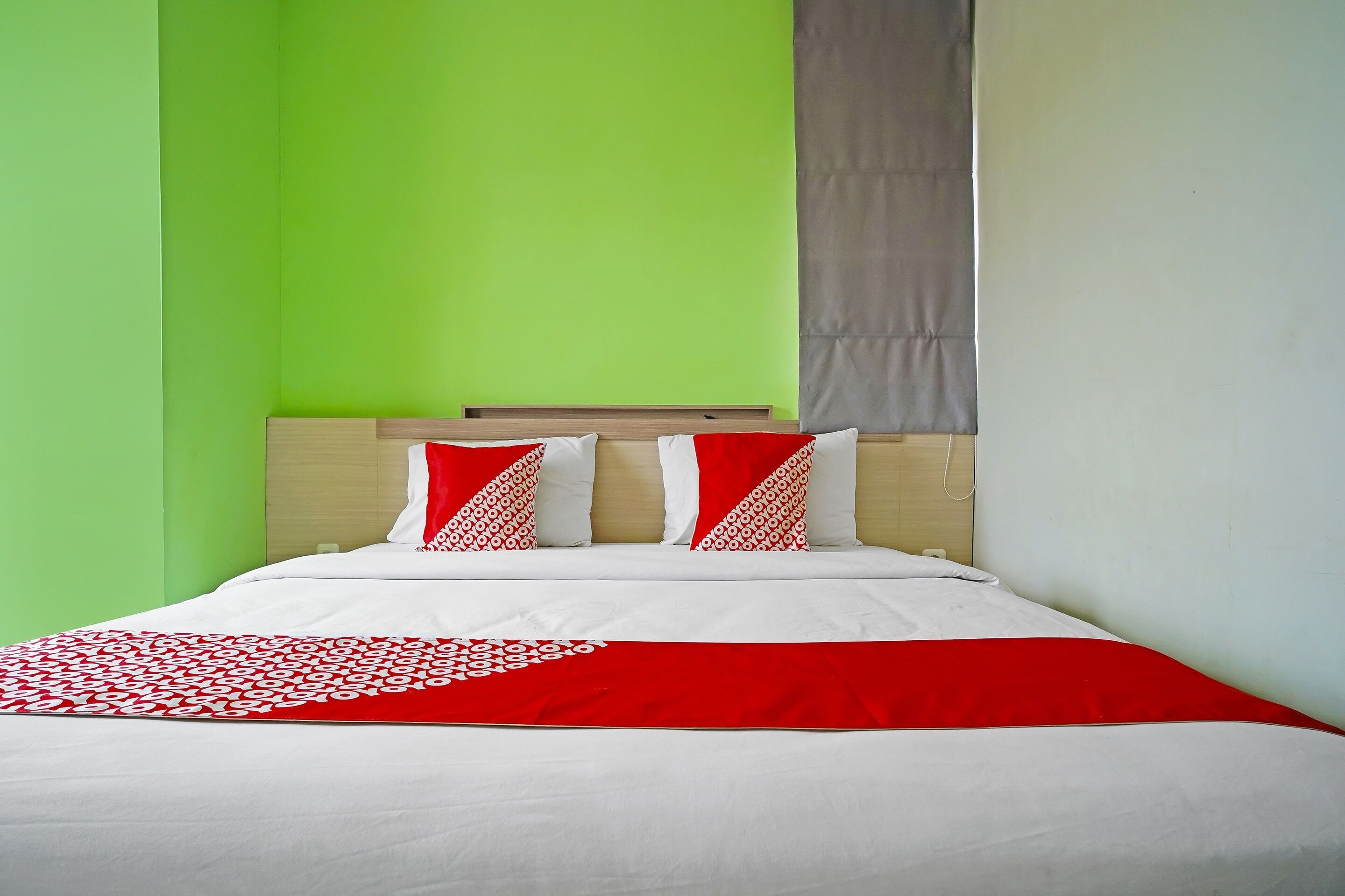 A bed with white and red bedding, a wooden headboard, and a green wall.