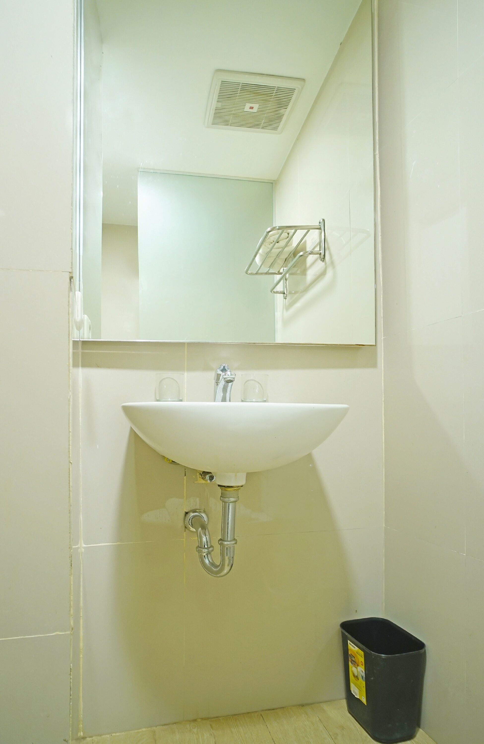 Une salle de bain avec un lavabo blanc, un miroir et une poubelle noire.