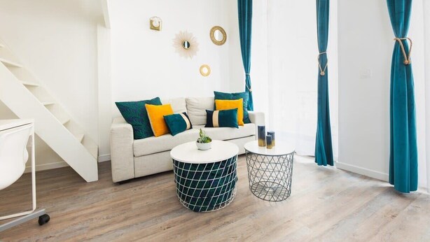 Una sala de estar moderna con un sofá blanco, cortinas turquesa y una escalera.