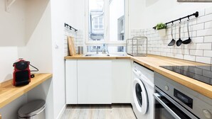 Cocina compacta con lavadora, horno empotrado y ventana con vistas a edificios.