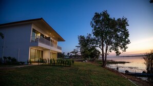 Una casa moderna de dos pisos con balcón, c ésped y vista al lago.