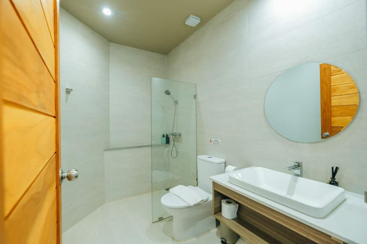 Ein modernes Badezimmer mit einer gläsernen Duschkabine, einer weißen Toilette, einem Waschbecken mit Spiegel und einer Holzausstattung.