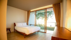 Un dormitorio con cama de madera, una mesita de noche pequeña y vista a un área verde a través de una puerta corrediza de vidrio.