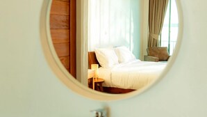 Un espejo redondo refleja un dormitorio con cama, cortinas y una mesita de noche.