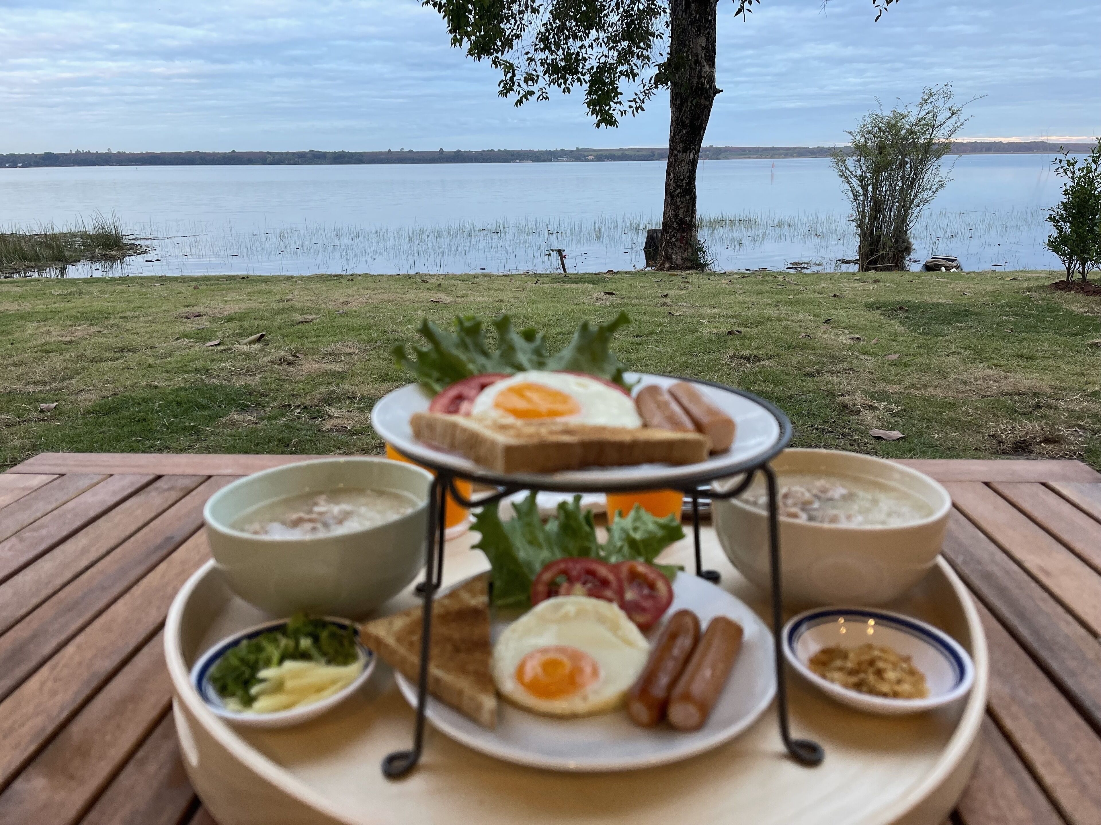 Un montaje para picnic con comida y bebidas sobre una mesa de madera junto a un lago.