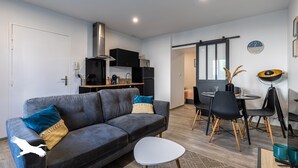 A modern living room with a grey sofa, a small white table, and a dining area with black chairs and a round table. - Le Besson Bey - Appartement de Standing T2 (Angoulême)
