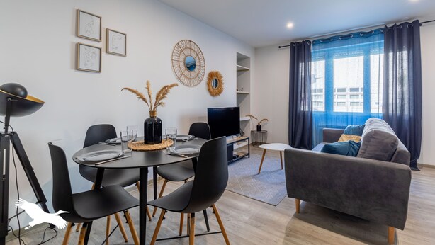 A modern living room with a dining area, a sofa, a TV, and artwork on the wall. - Le Besson Bey - Appartement de Standing T2 (Angoulême)