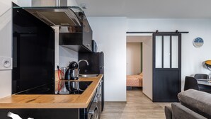 A compact kitchen with a wooden countertop, a black stove, and a sliding door leading to a dining area. - Le Besson Bey - Appartement de Standing T2 (Angoulême)