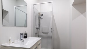 A modern bathroom with a white sink, mirror, and glass shower enclosure. - Le Besson Bey - Appartement de Standing T2 (Angoulême)