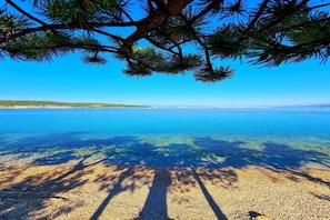 A beach with clear water, pebbles, and a tree casting shadows. - Apartment in Šilo on Krk Island (Šilo - Krk)