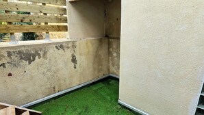 Un petit patio clos, doté d’une pelouse artificielle, d’un banc en bois et d’un toit recouvert de tuiles.