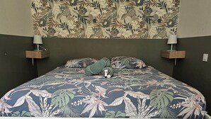 Un lit recouvert d’une couvre-lit à motifs floraux, deux tables de chevet avec des lampes et un mur orné d’un papier peint à motifs floraux.
