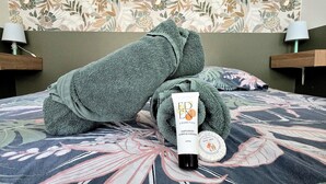 Un lit recouvert d’une couvre-lit à motifs floraux, une serviette verte et un tube de lotion de la marque Eden Cosmetics.