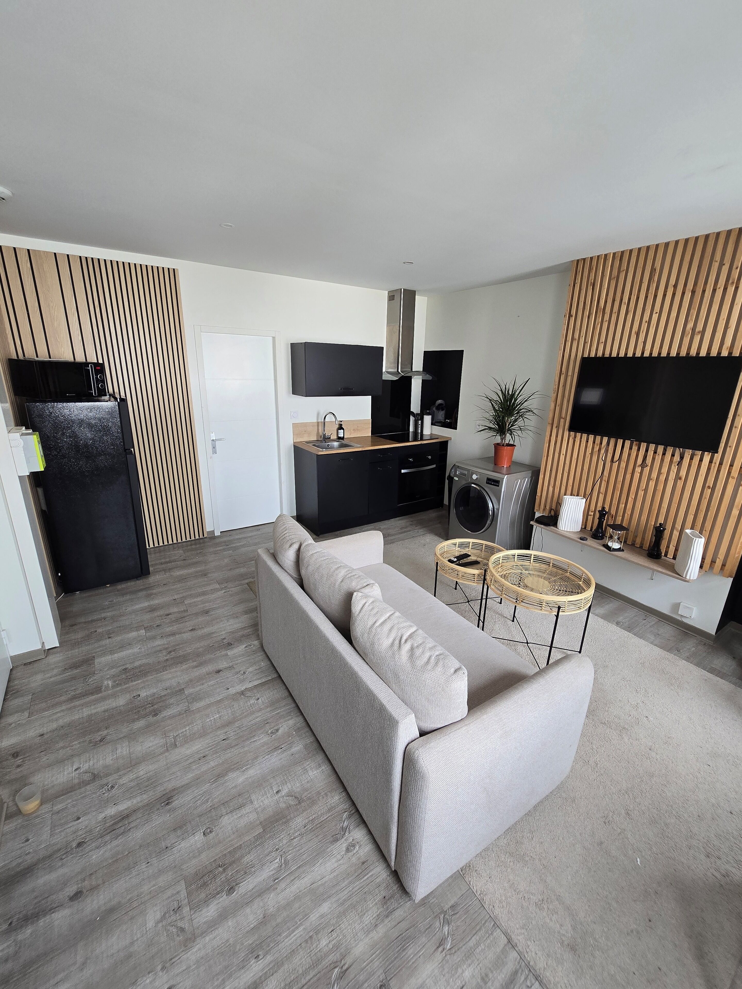 A modern living room with a sofa, a dining area with a kitchen in the background, and a flat-screen TV mounted on the wall.