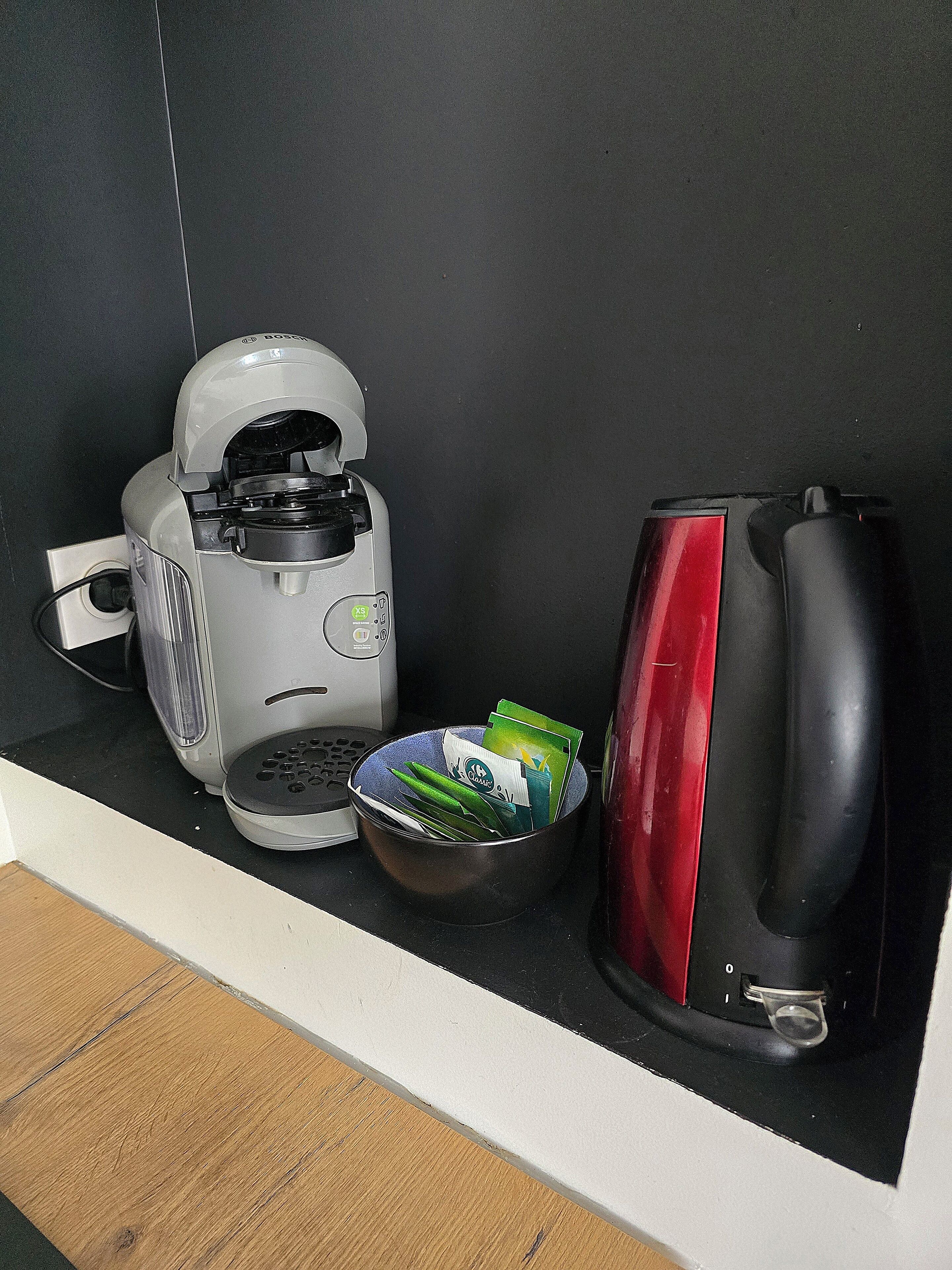 A kitchen with a coffee maker, a kettle, and a bowl of green vegetables.