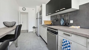 Une cuisine moderne avec des meubles de couleur noire, un lave-vaisselle et un plan de travail agrémenté d’ustensiles de cuisine.
