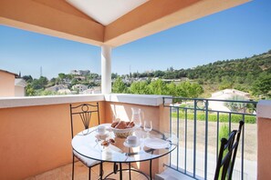 Un balcon avec une table dressée pour deux personnes, donnant sur une colline parsemée de bâtiments.