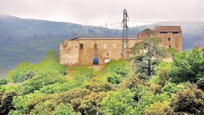 Ein historisches Steinhaus mit einem Glockenturm, umgeben von üppiger Vegetation und Hügeln im Hintergrund.