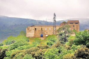 Ein historisches Steinhaus mit einem Glockenturm, umgeben von üppiger Vegetation und Hügeln im Hintergrund.
