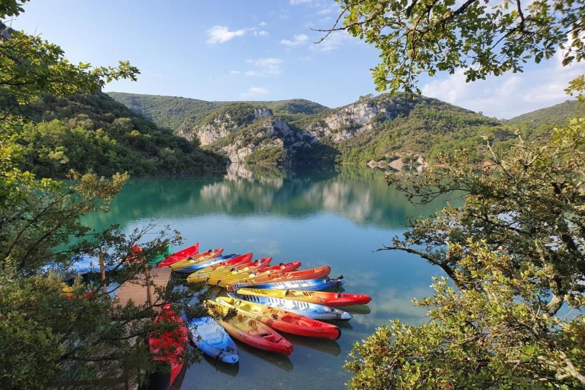 Un lago sereno rodeado de colinas, con una hilera de kayaks de colores amarrados en la orilla.