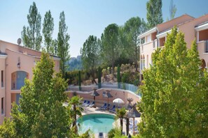 Un espace piscine doté de chaises longues et de parasols, entouré d’arbres et d’immeubles.