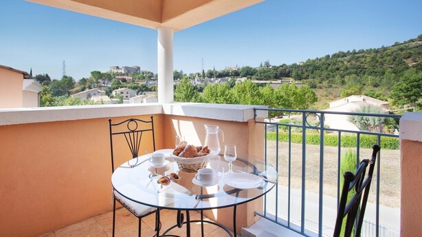 A balcony with a table set for two, overlooking a hillside with buildings. - Apartment in Gréoux-Les-Bains near Lakes (Gréoux-les-Bains)