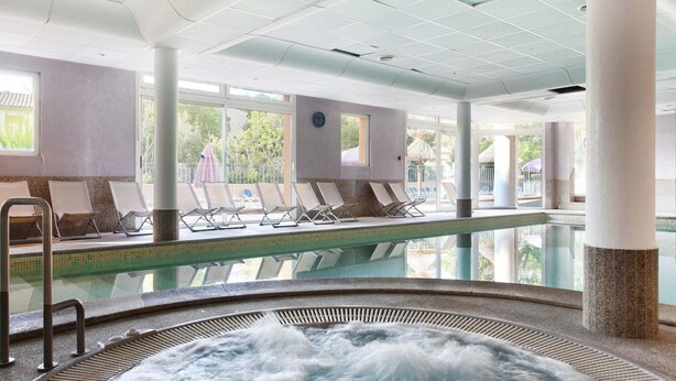 Zona de piscina con sillas de descanso, un jacuzzi y vistas al exterior.