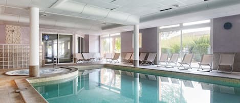An indoor swimming pool with lounge chairs and a view of the outdoors.