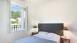 Un dormitorio con una cama, dos mesitas de noche con lámparas, un ventanal con vistas a zonas verdes y un balcón.