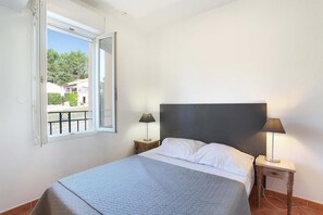 Ein Schlafzimmer mit einem Bett, zwei Nachttischen mit Lampen, einem Fenster mit Blick ins Grüne und einem Balkon.