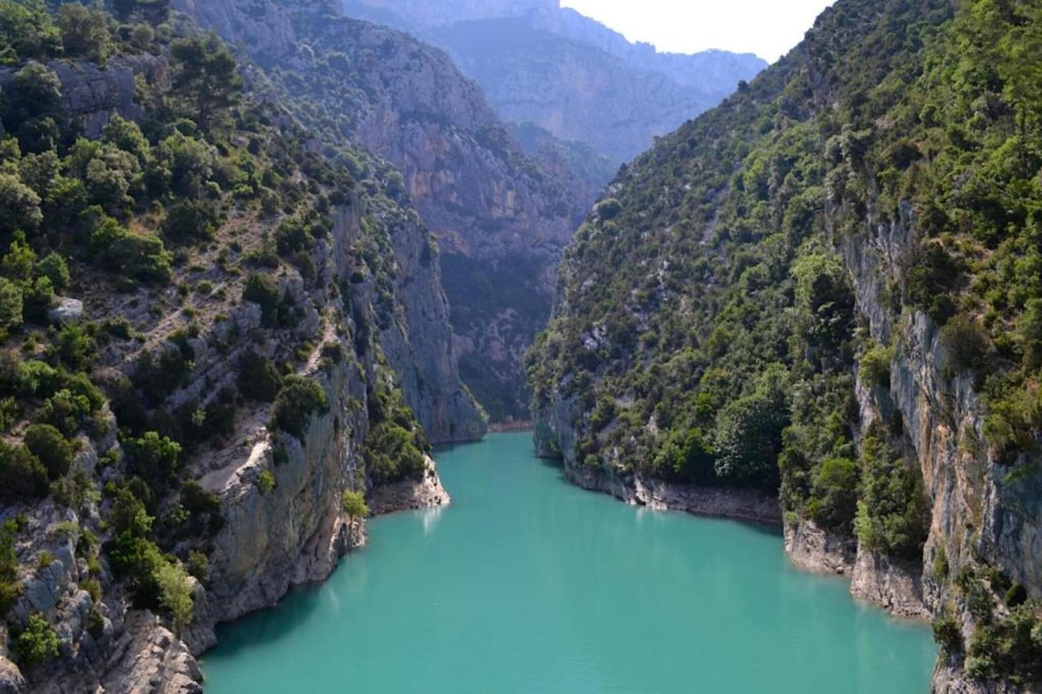 A canyon with a turquoise river, steep cliffs, and dense greenery.