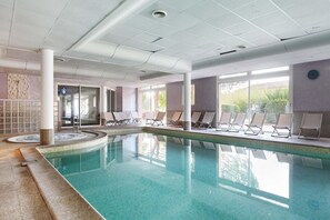 Ein Hallenbad mit Liegestühlen und Blick ins Freie.
