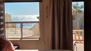 Una habitación con un ventanal grande que da a una playa, una cama y una mesita.